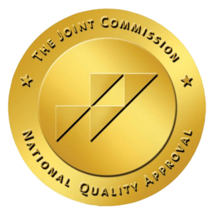 A gold circular seal with "The Joint Commission National Quality Approval" around the edge and a stylized geometric logo in the center.
