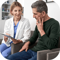 A female healthcare professional shows a digital tablet to an older man who is touching his face, possibly discussing his symptoms during a medical consultation.