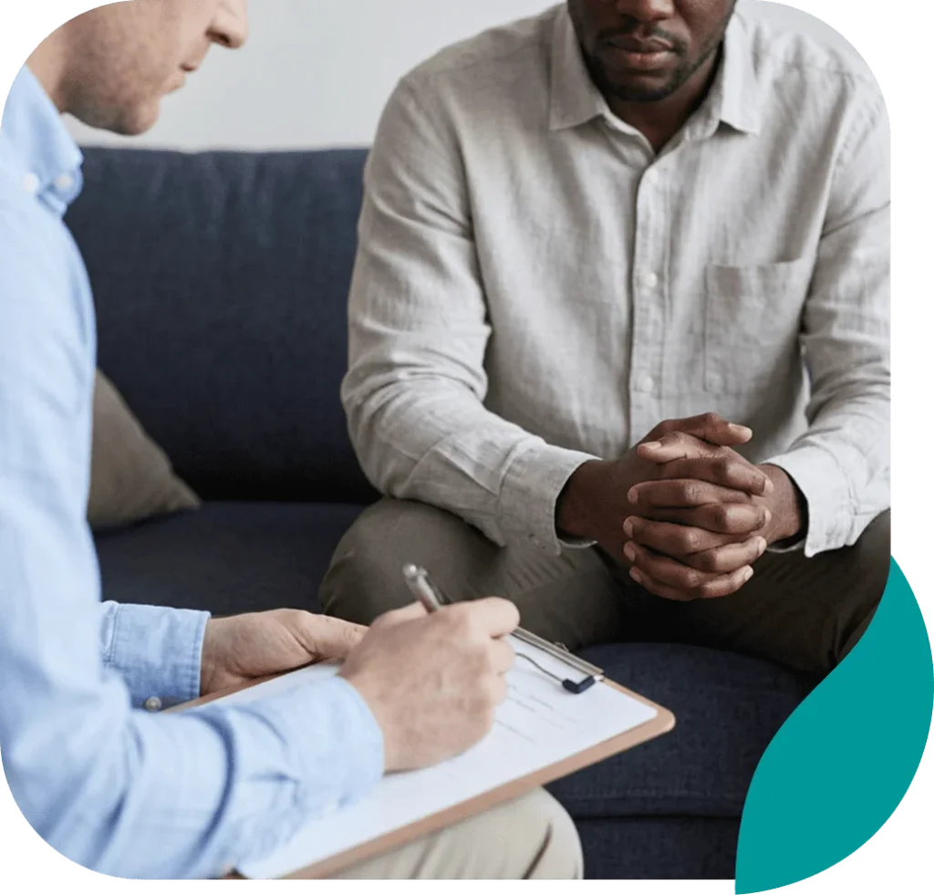 Client with clasped hands during a therapy session as the therapist takes notes